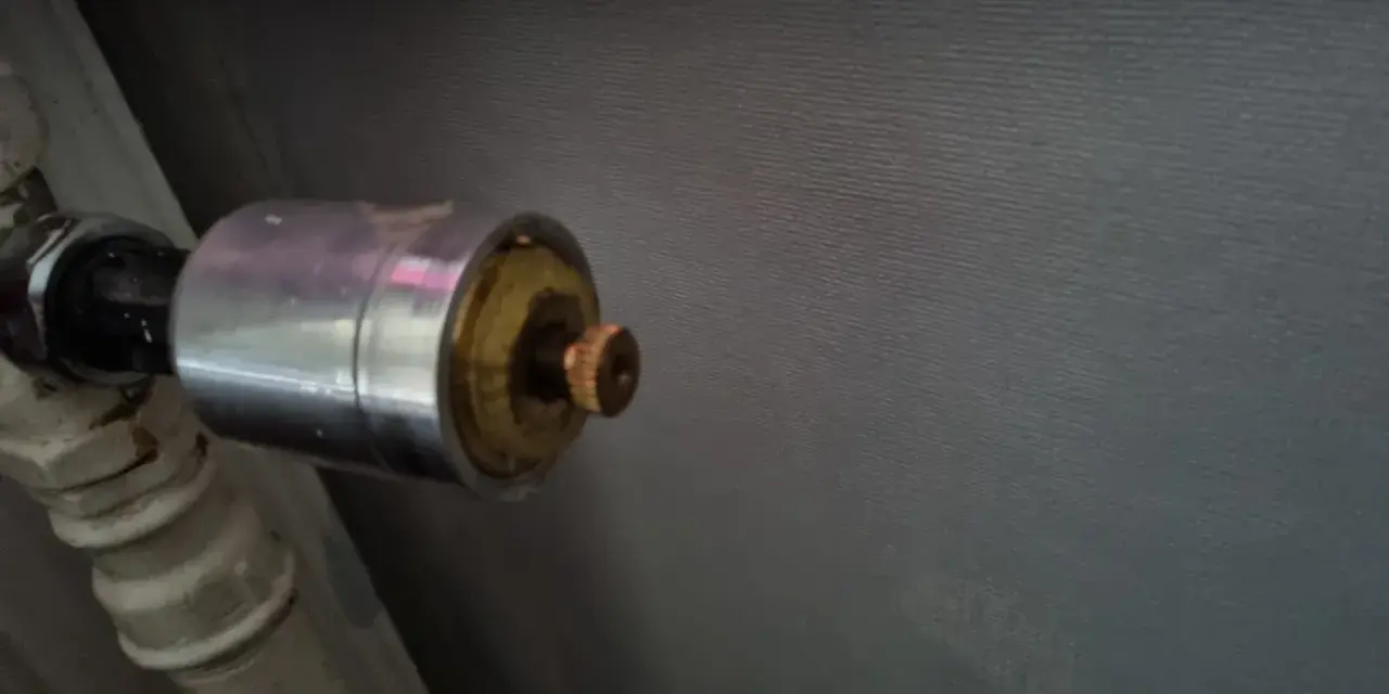 En gammal AGA termostat på ett element. Den kromade delen har en mässingsfärgad ratt.