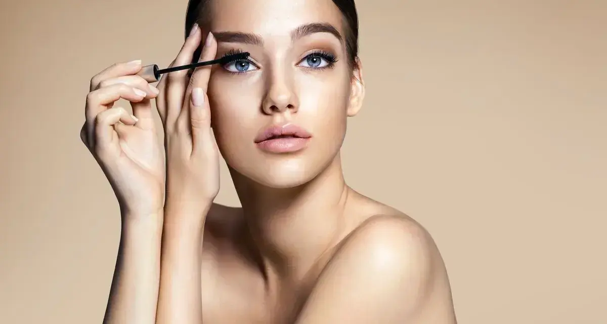Donna con occhi azzurri applica mascara. Scopri come togliere il mascara waterproof senza irritare la pelle.