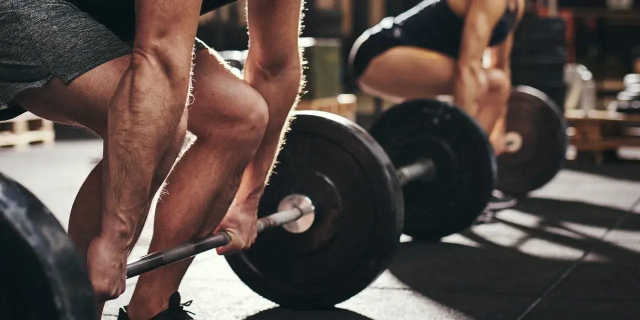 Personer lyfter skivstång i gym. Frågan "hur lång tid tar det att bygga muskler" besvaras med konsekvent träning.