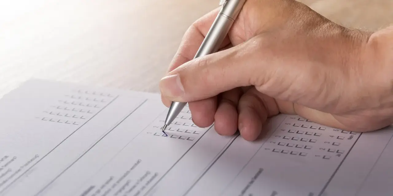Dłoń z długopisem wypełnia formularz, zaznaczając odpowiedzi. To część procesu tworzenia wykazu majątku.