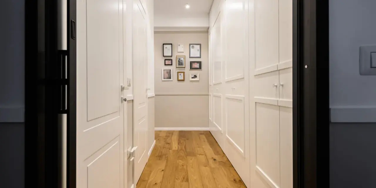 Corridoio con parquet e armadi bianchi. Un'idea per come dividere un corridoio lungo con porte e quadri decorativi.
