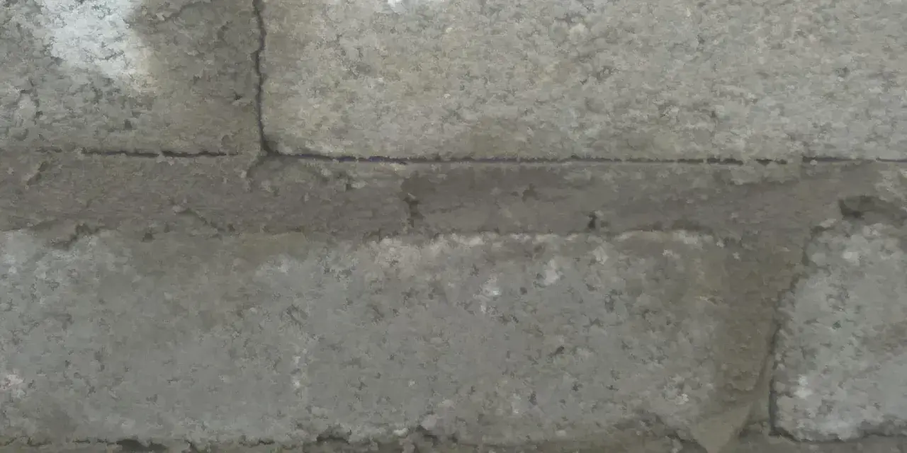 Widok z bliska na ścianę z bloczków betonowych, pokazujący grubość spoiny między nimi.