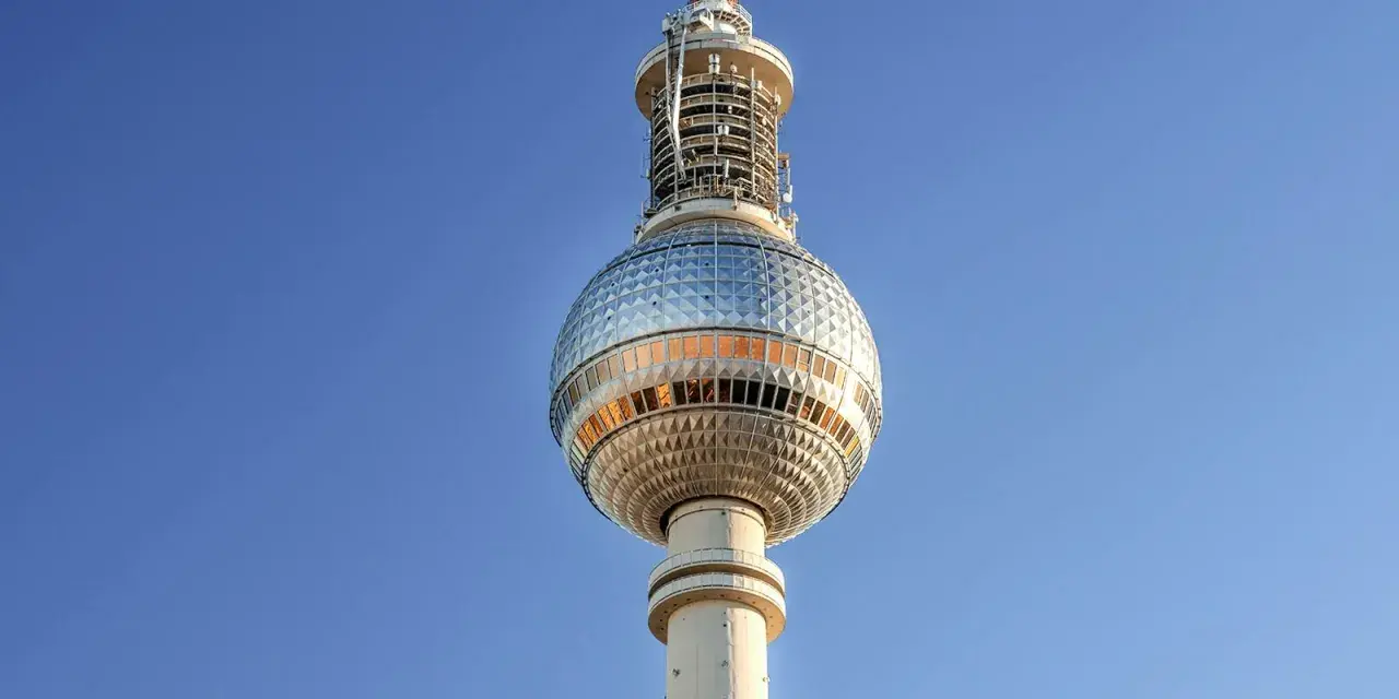 Die Torre della televisione di Berlino ragt in den blauen Himmel. Ihre kugelförmige Spitze mit Fenstern reflektiert das Licht.