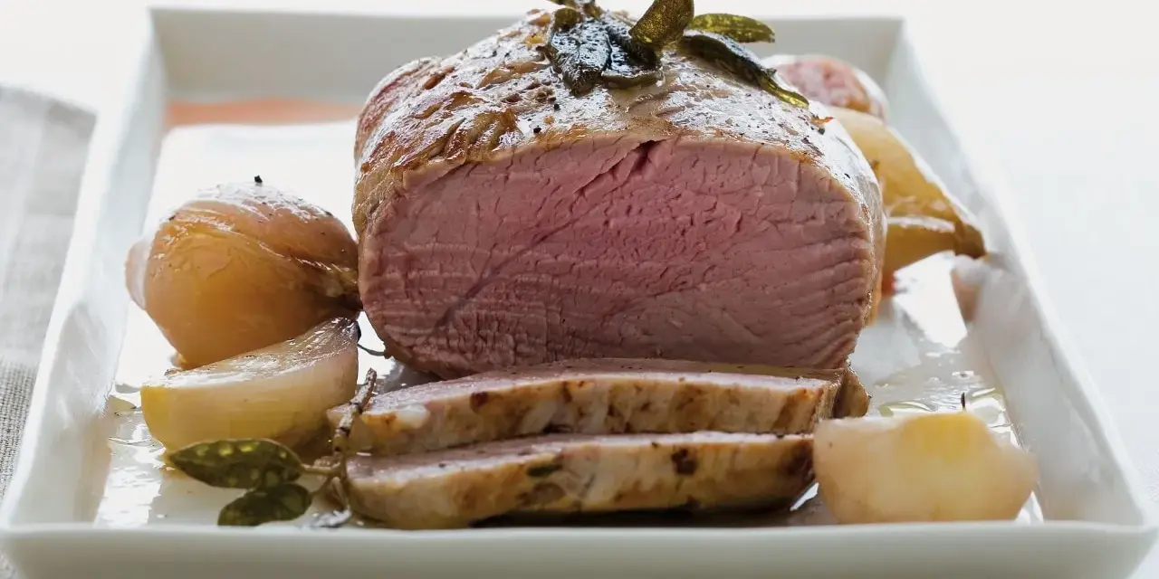Succulento filetto al forno, cotto alla perfezione con cipolle e erbe aromatiche, servito su un piatto bianco.