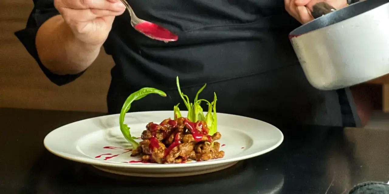 Chef decora un piatto di straccetti di manzo con una salsa rossa brillante, guarnendo con verdure verdi.