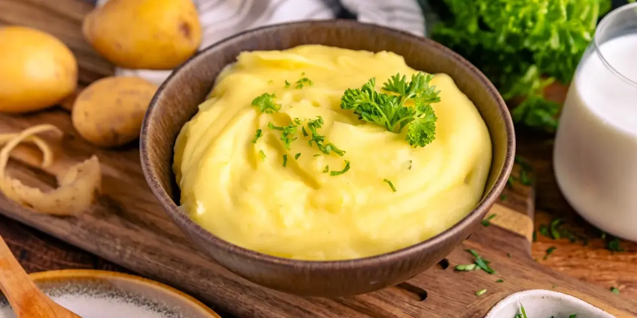 Cremiger Kartoffelbrei, perfekt zubereitet im Thermomix, garniert mit Petersilie. Dazu frische Kartoffeln und ein Glas Milch.
