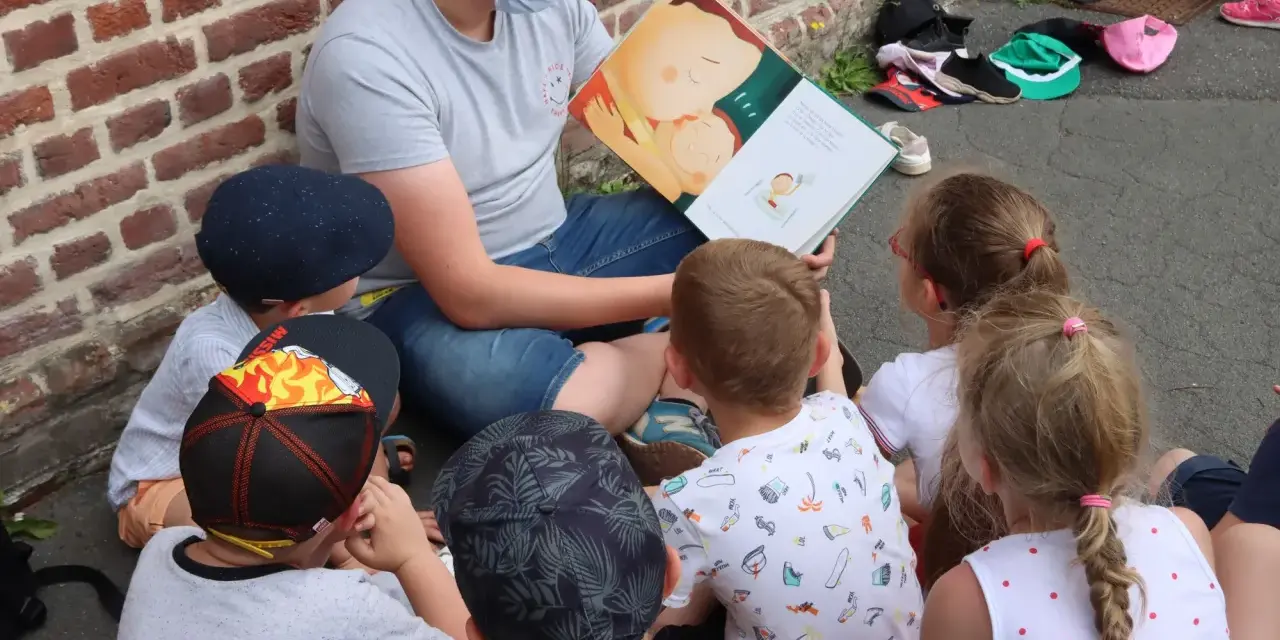 Un animateur lit un livre illustré à des enfants assis en cercle. L'image évoque un moment de partage et d'apprentissage, comme un diplôme animation.