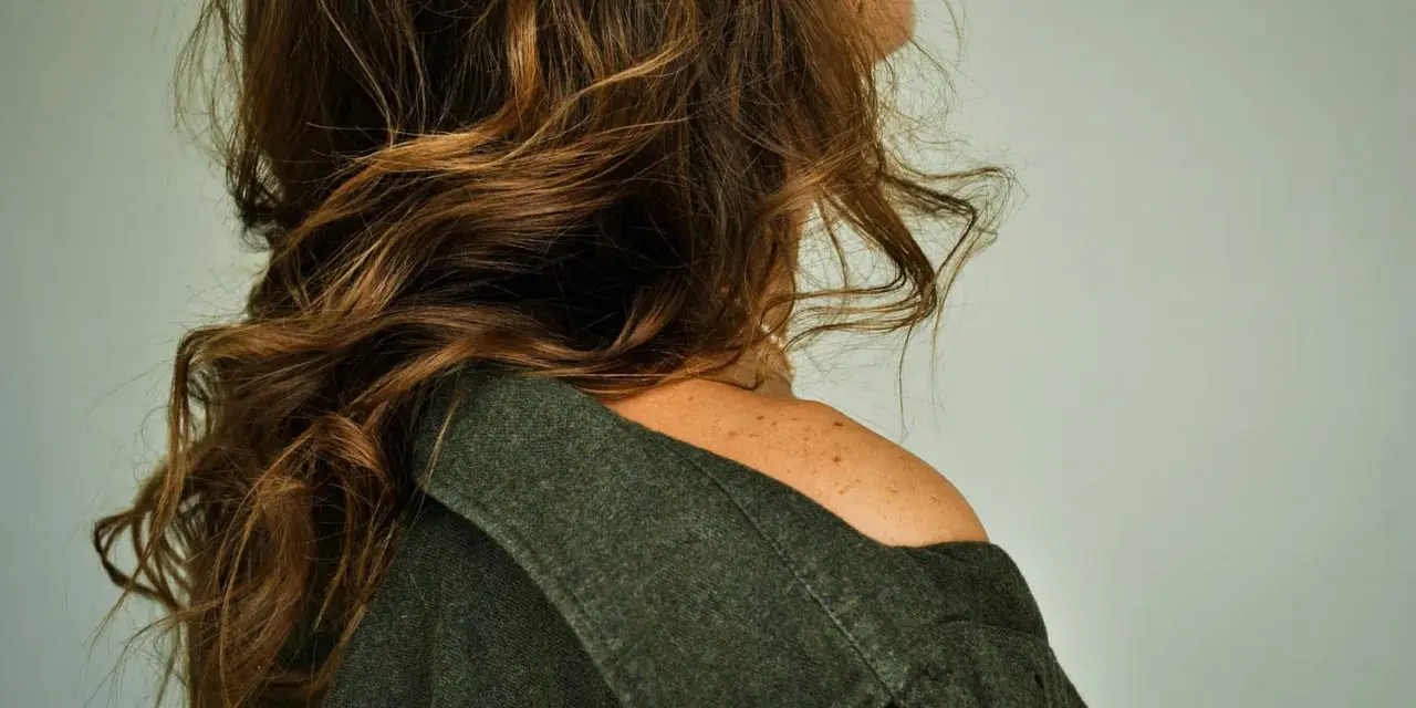 Spalle scoperte e capelli castani mossi, un dettaglio di donne con pochi capelli che incornicia il volto.