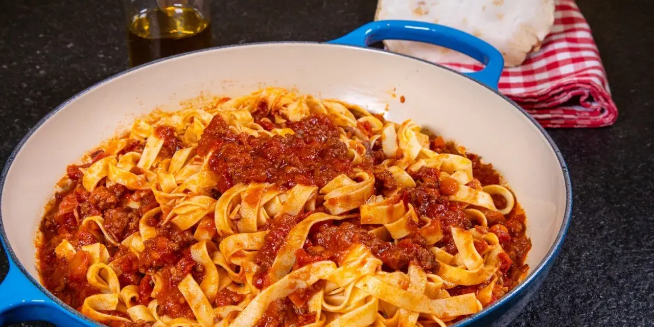 Herzhafte Tagliatelle mit einer reichhaltigen alla bolognese Sauce in einer blauen Pfanne, bereit zum Servieren.