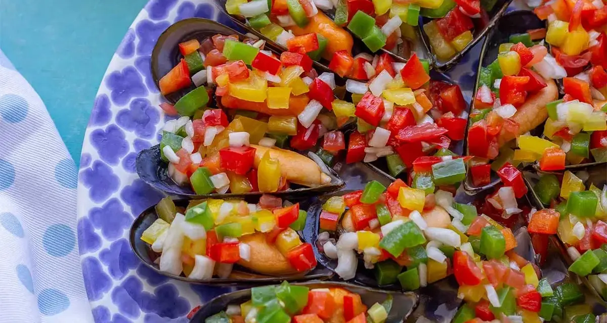Mejillones a la vinagreta, cubiertos con una colorida mezcla de pimientos y cebolla picados. Un plato fresco y vibrante.