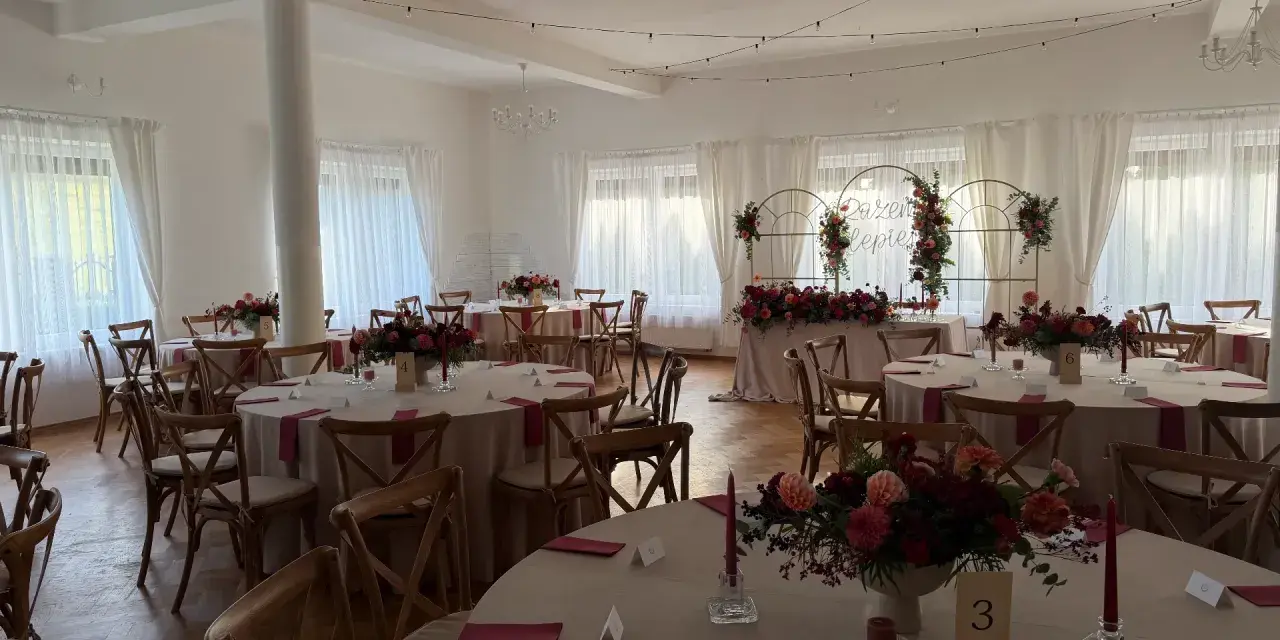 Elegancka sala weselna z okrągłymi stołami, kwiatami i świecami. Idealne miejsce, by wybrać najlepszą salę na wesele.