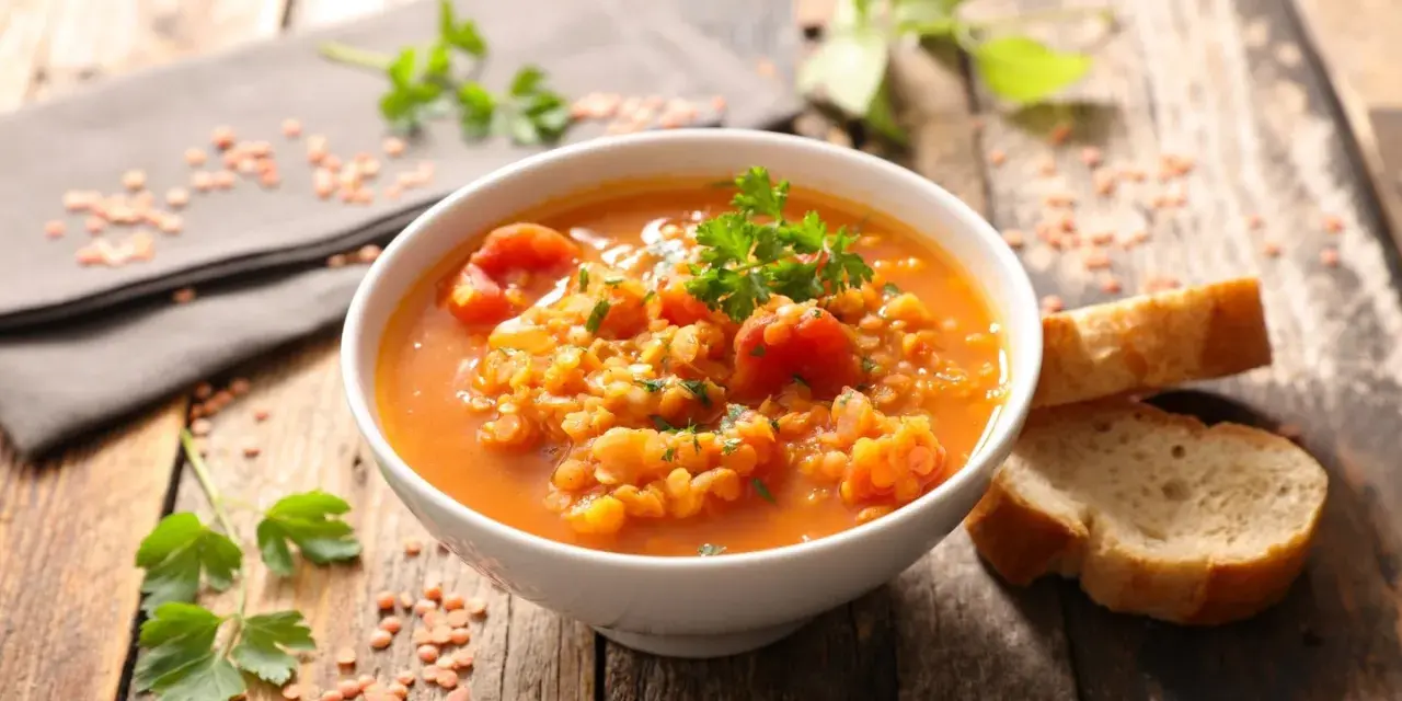 Eine dampfende Schüssel mit herzhafter rote linsensuppe, garniert mit Petersilie, daneben knuspriges Brot auf rustikalem Holztisch.
