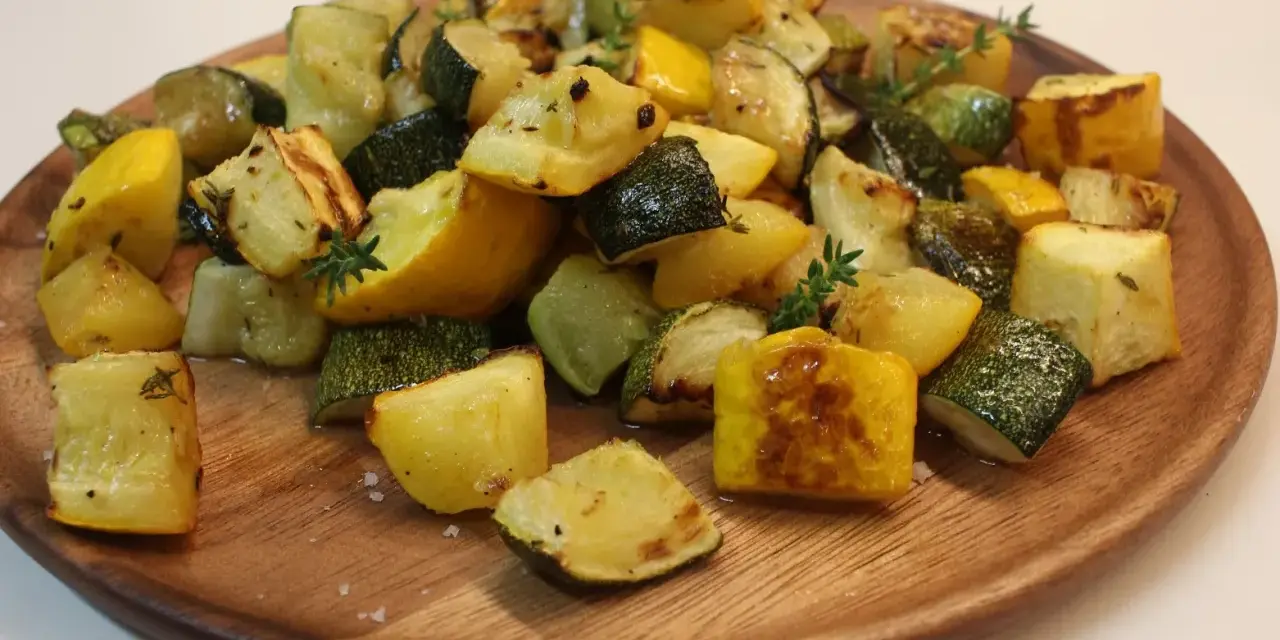 Délicieux courgettes au four, coupées en dés et parsemées de thym frais sur un plat en bois.