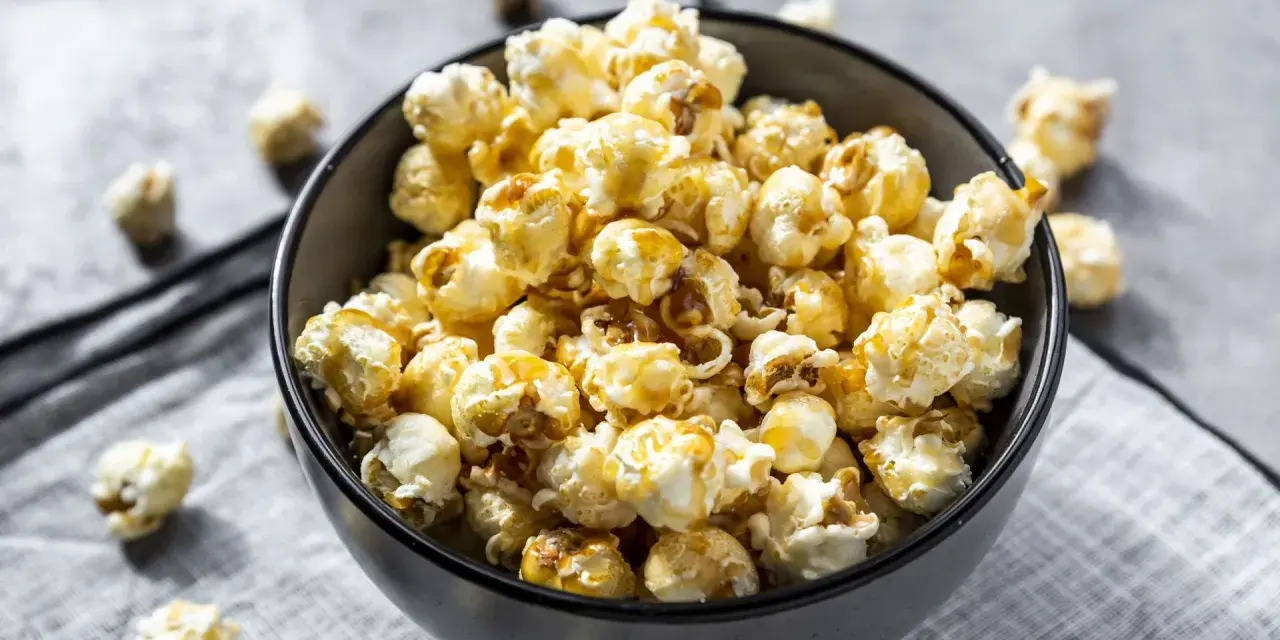 Un bol rempli de pop corn sucré, avec quelques grains éparpillés autour. Un délice croustillant pour une soirée cinéma.