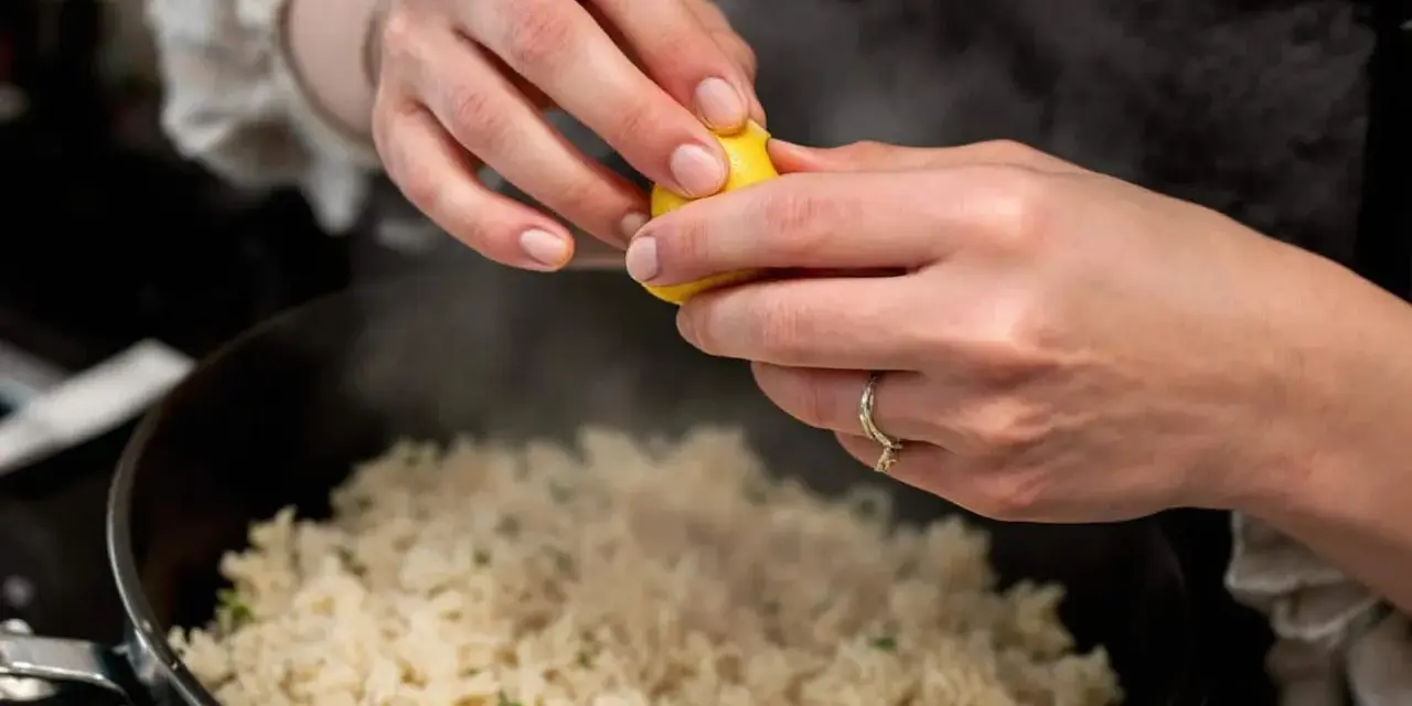Des mains pressent un citron sur une soupe de riz fumante, ajoutant une touche de fraîcheur à ce plat réconfortant.