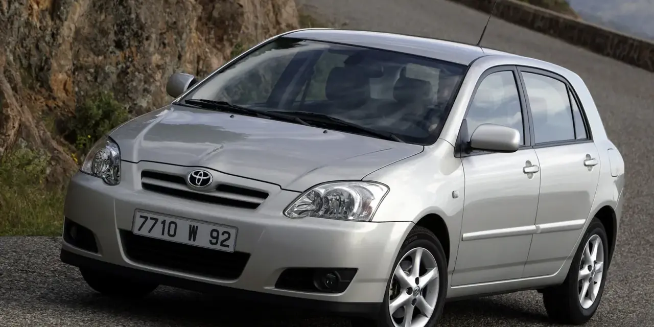 Srebrna Toyota Corolla E12 na krętej drodze, z kamienistym zboczem w tle.