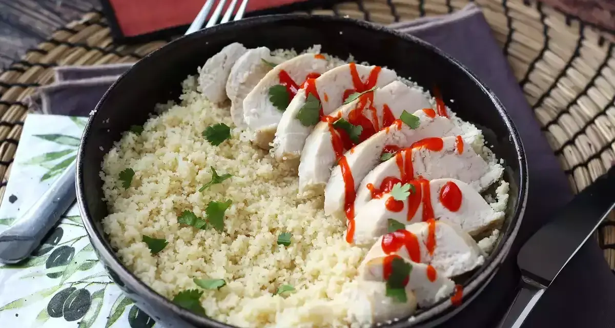 Delizioso petto di pollo in padella, affettato e servito su un letto di couscous, guarnito con prezzemolo e un filo di salsa piccante.