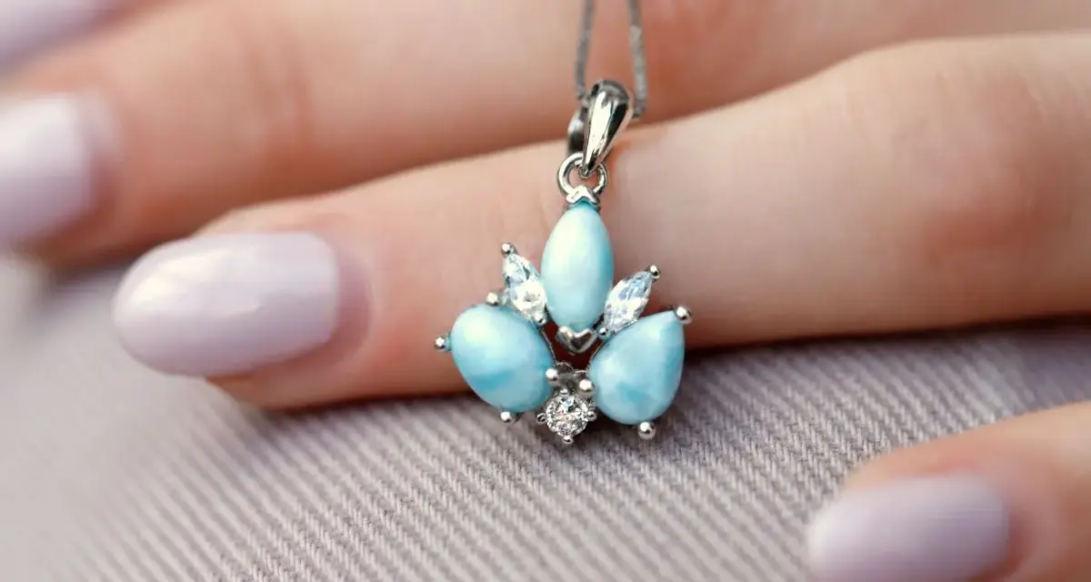 Un ciondolo con una splendida larimar pietra, incastonata con zirconi, adagiato su una mano con unghie lilla.