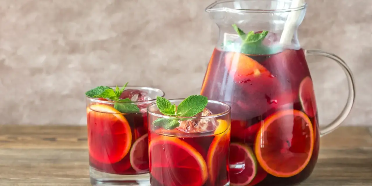 Dwa szklanki i dzbanek pełne orzeźwiającej Sangrii czerwonej z plasterkami pomarańczy i limonki, ozdobione miętą. Idealny wybór na lato!