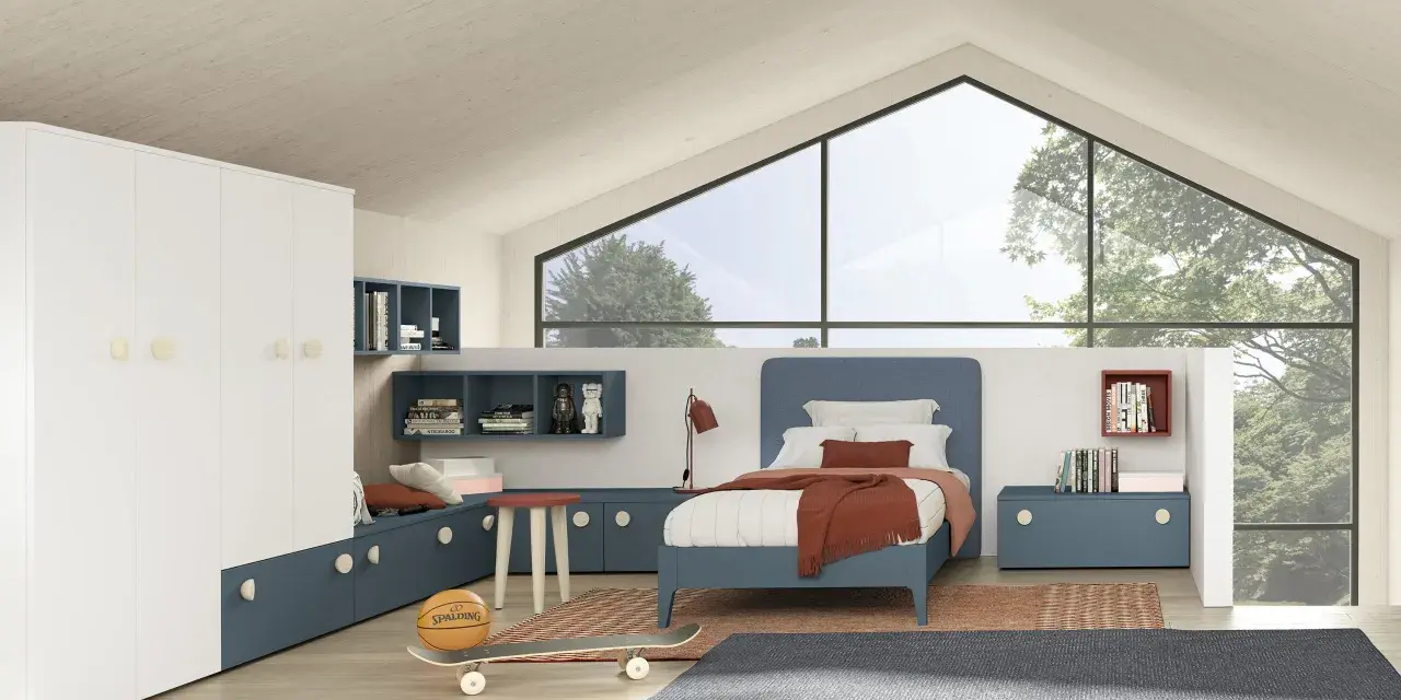 Un accogliente **letto sotto la finestra** in una stanza moderna, con armadio bianco, librerie blu e un pallone da basket.