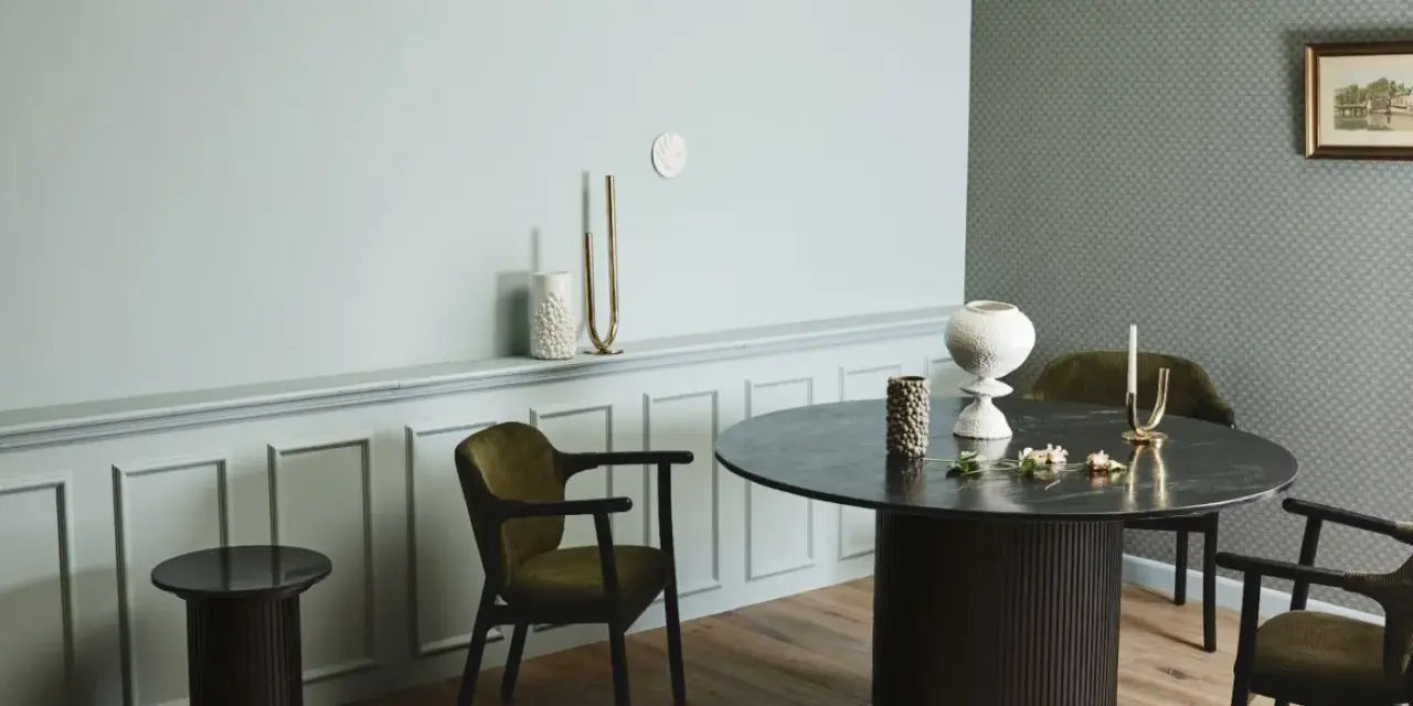 Ett runt matbord med mörka stolar skapar en inbjudande atmosfär. Utrymme runt matbordet ger plats för samtal och gemenskap.