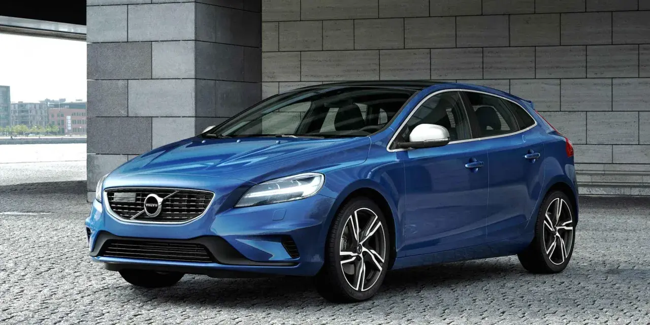 Niebieskie Volvo V40 D2 z czarnym dachem, zaparkowane na kamiennej nawierzchni, z nowoczesną architekturą w tle.