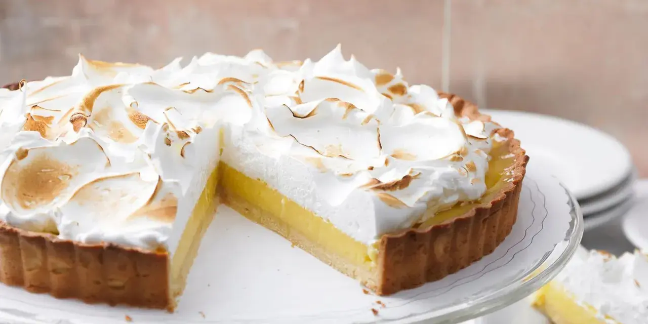Eine köstliche Tarte au Citron mit fluffiger Baiserhaube, die auf einem Tortenständer präsentiert wird.