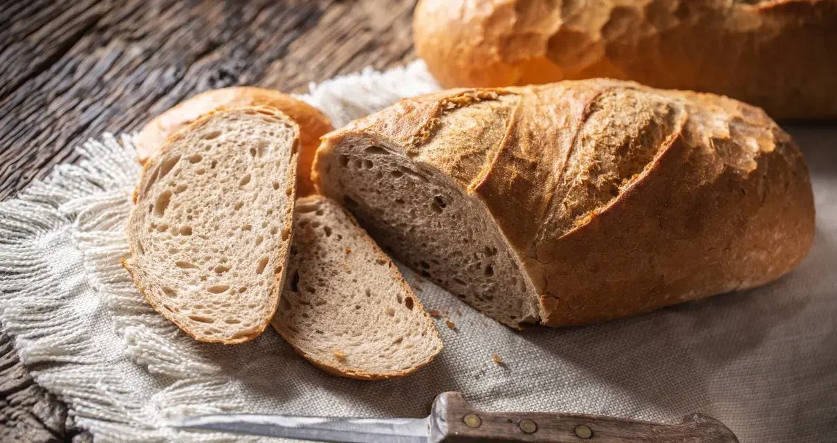 Chleb z kaszy jaglanej, pokrojony na kromki, leży na lnianej serwetce obok noża.