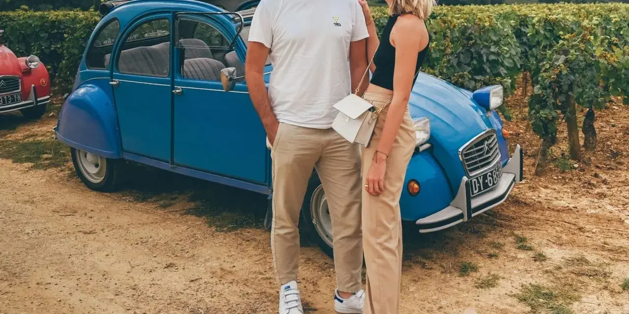 Couple souriant devant une 2CV bleue dans les vignes, une belle idée pour visiter Beaune en 1 jour.