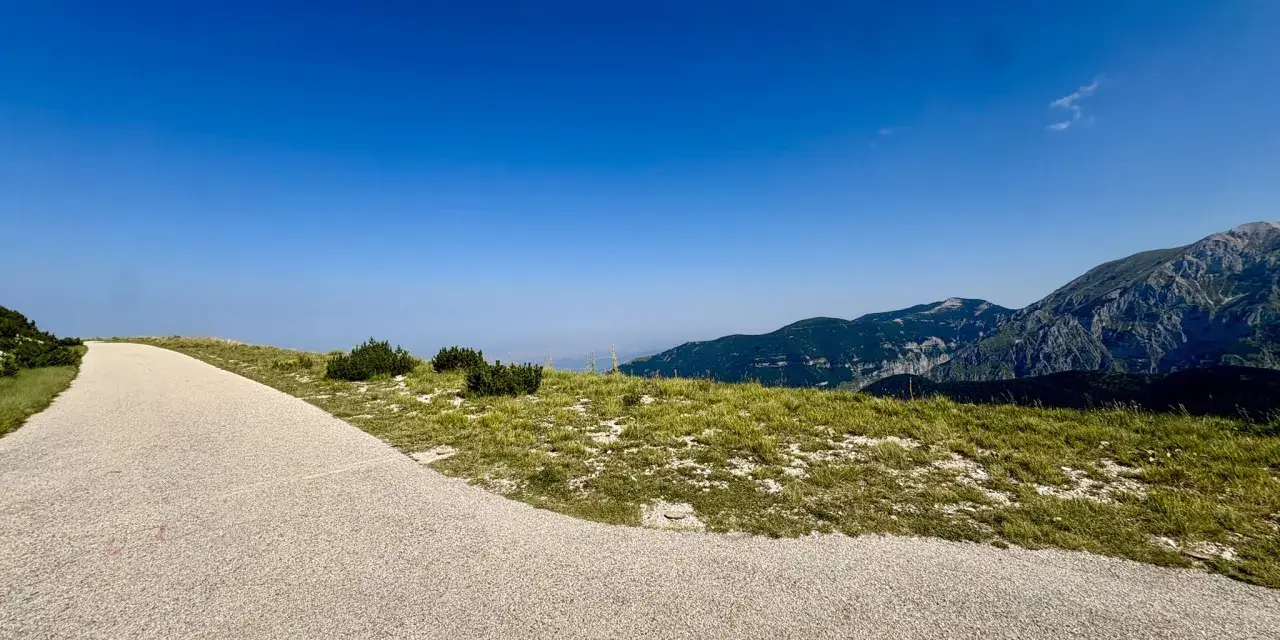 Sentiero ghiaioso verso la cima Blockhaus, con prati verdi e montagne sullo sfondo sotto un cielo azzurro.