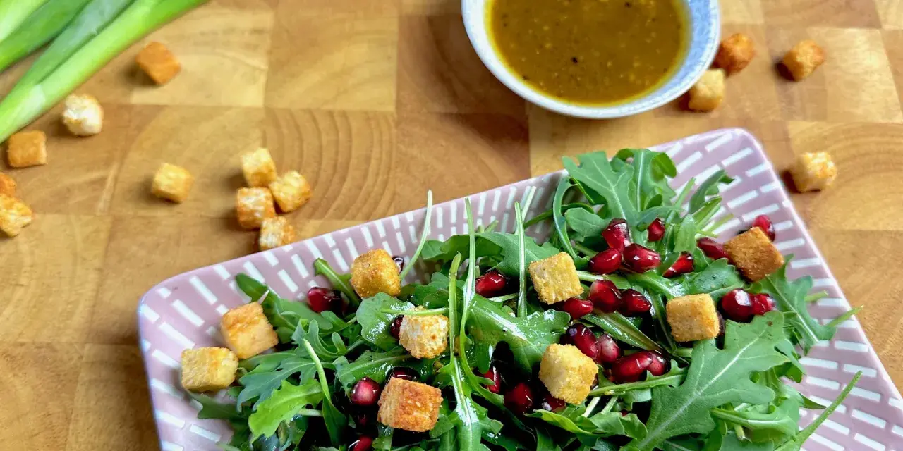 Frischer Rucola Salat mit Granatapfelkernen und Croutons, dazu ein Dressing.