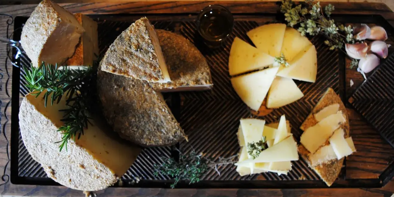 Tabla de quesos variados, hierbas aromáticas y ajos sobre madera.