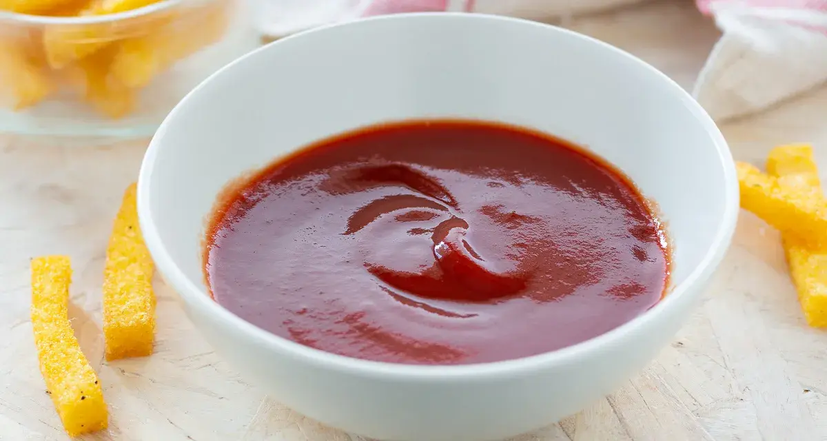 Una ciotola di ketchup fatto in casa, pronto per intingere bastoncini di polenta dorati.