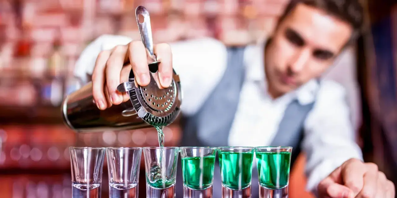 Barman nalewa zielony alkohol do kieliszków.