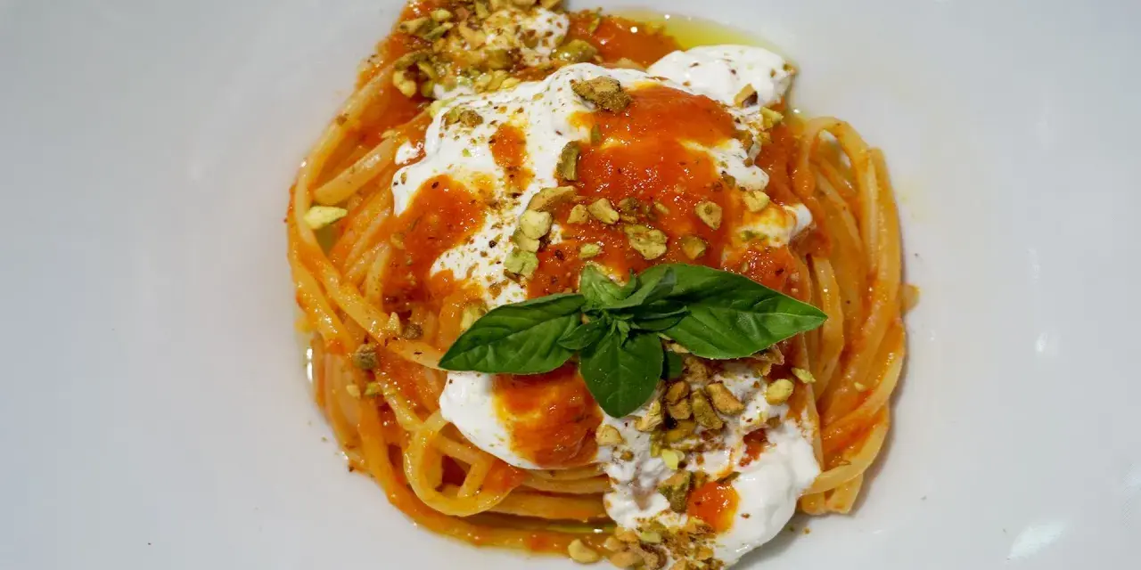 Un piatto invitante di pasta con stracciatella, salsa di pomodoro, pistacchi tritati e una foglia di basilico fresco.