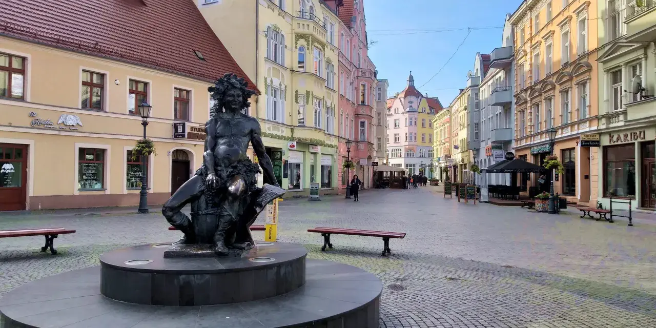 Fontanna z postacią Baccha na brukowanym placu, otoczona kolorowymi kamienicami. Zielona Góra atrakcje turystyczne.
