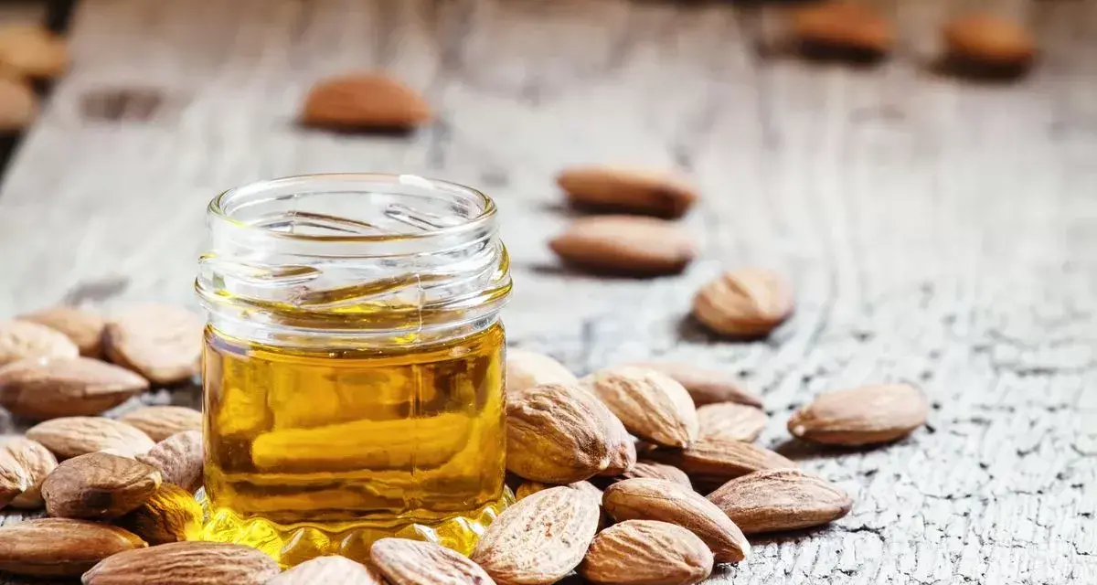 Aceite de almendras para que sirve: un frasco de aceite dorado rodeado de almendras sobre madera rústica.