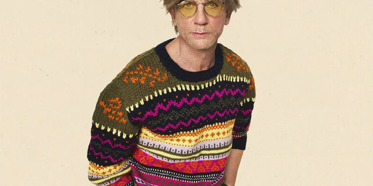 Mann mit gelber Brille trägt einen bunten Pullover aus Wolle, schleudern von Mustern.
