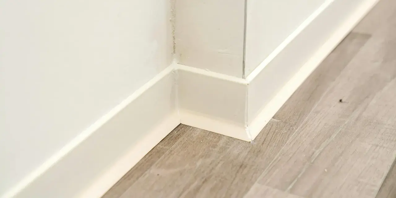 Angolo di una stanza con parquet grigio e battiscopa bianco appena installato.