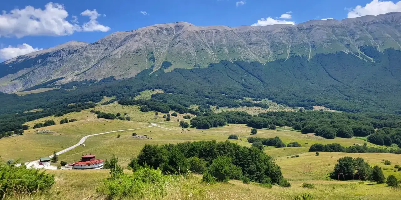 Vasta distesa verde ai piedi del monte Mileto, con un edificio circolare rosso e una strada tortuosa.