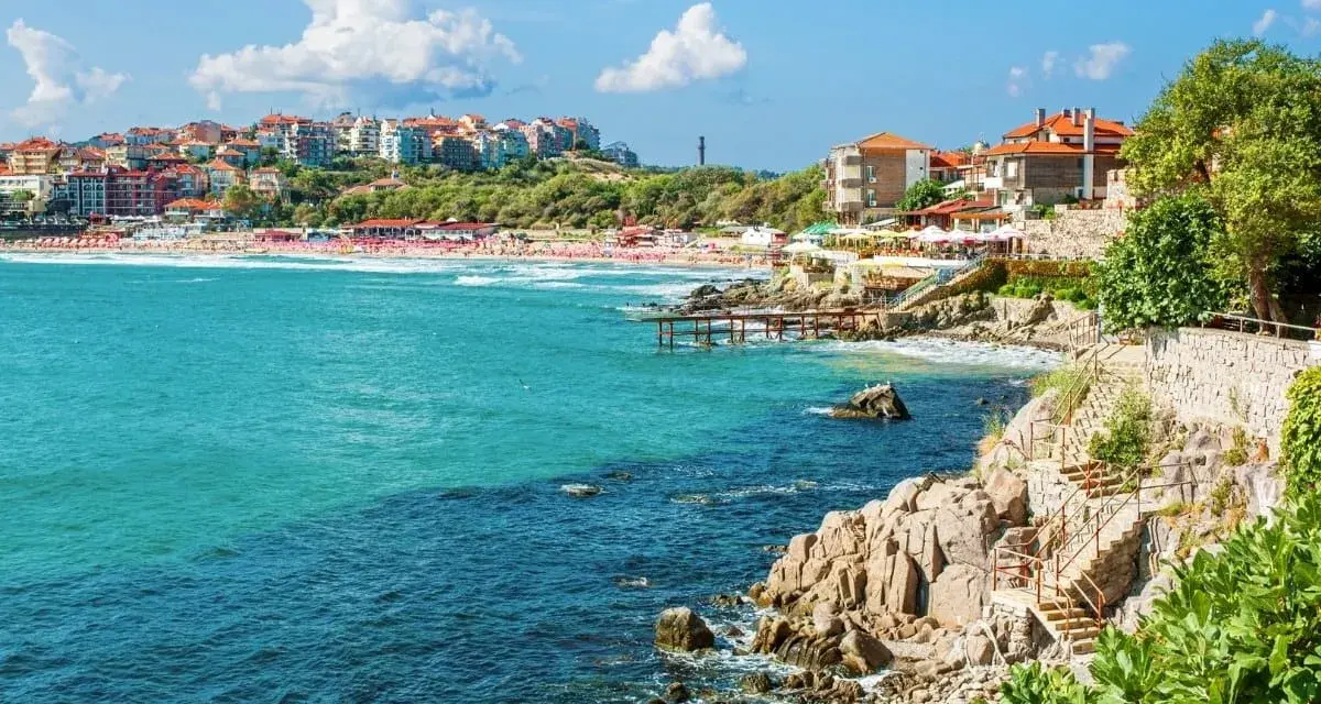 Słoneczna plaża i turkusowe morze w Bułgarii. Widok na miasteczko z czerwonymi dachami i skaliste wybrzeże z kamiennymi schodami. Atrakcje turystyczne nad Morzem Czarnym.