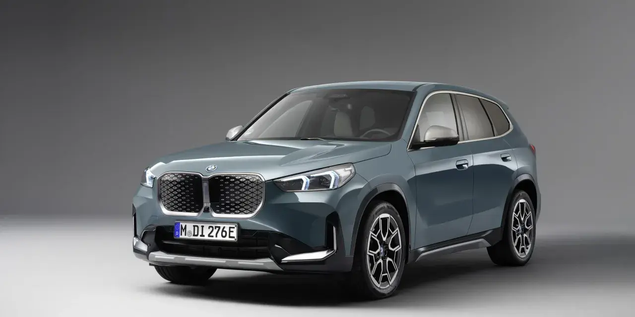 BMW iX1 w kolorze zielonym, widok z przodu, na szarym tle.