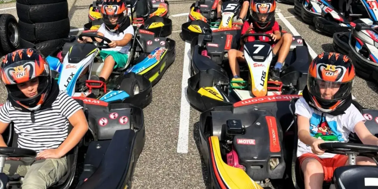 Des enfants casqués prêts pour une course de colo karting, le sourire aux lèvres, impatients de démarrer.