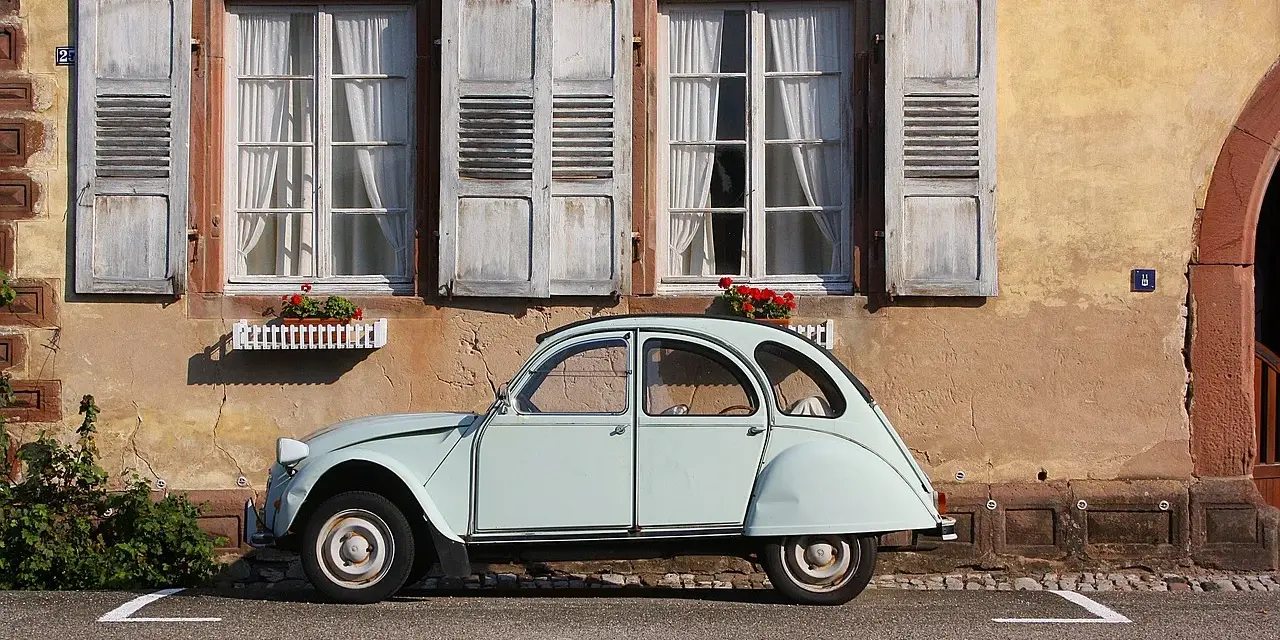 Jasnoniebieski, zabytkowy Citroen 2CV, jeden z klasycznych modele stare, parkuje przed kamiennym domem z drewnianymi okiennicami.