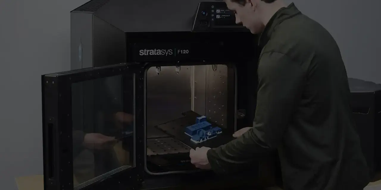 Mężczyzna wkłada wydrukowany model do drukarki 3D Stratasys F120. Tak wygląda drukarka 3d w akcji.