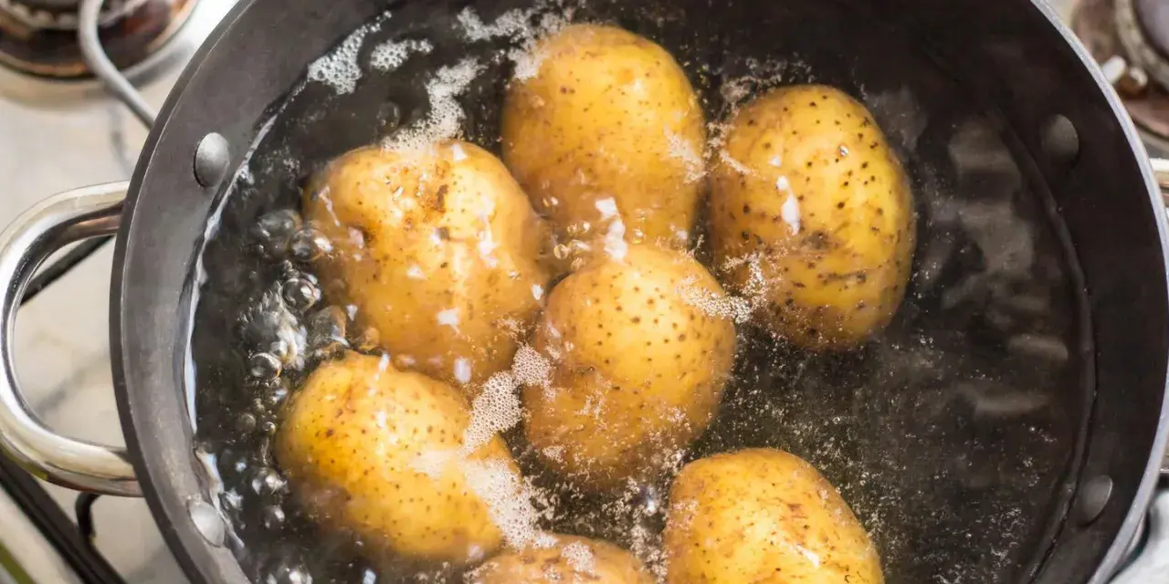 Mehrere ganze Kartoffeln kochen in einem Topf mit sprudelndem Wasser auf dem Herd.