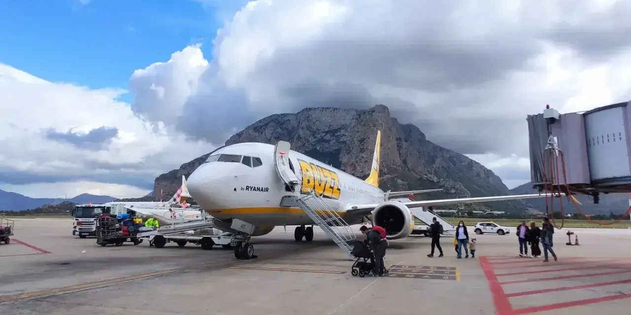 Samolot Buzz by Ryanair na lotnisku na Sycylii, z górami w tle.