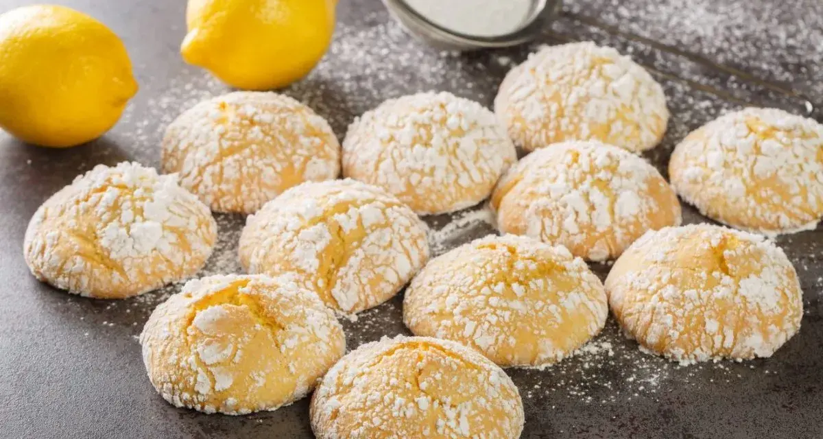 Deliziosi biscotti al limone spolverati di zucchero a velo, con limoni freschi sullo sfondo.