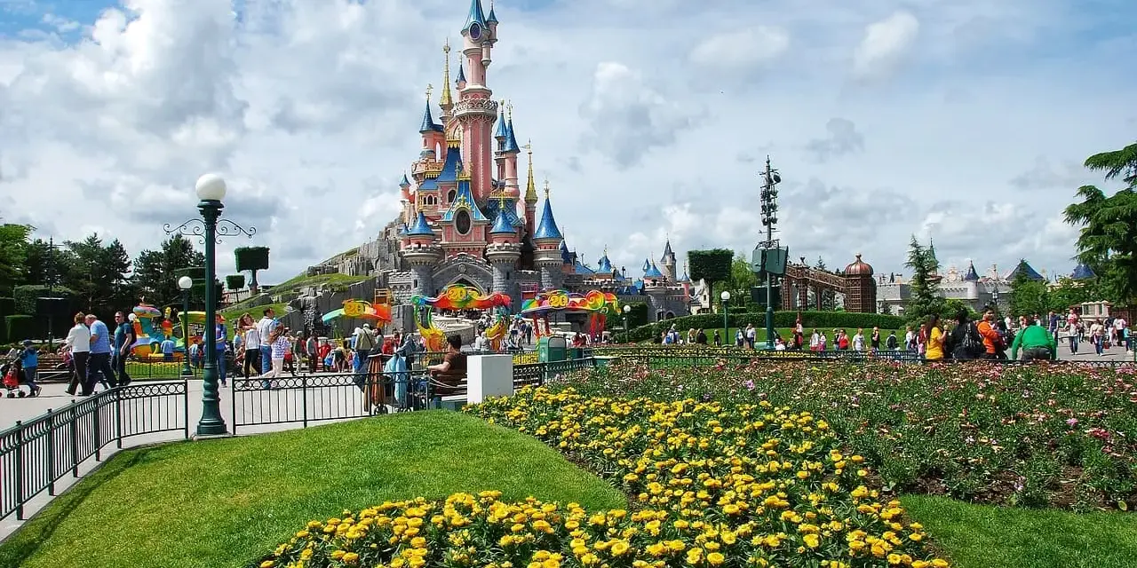 Disneyland Paris castle with colorful flowers and crowds of people.