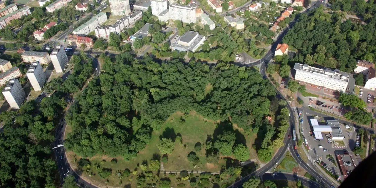 Widok z lotu ptaka na zielony park otoczony drogami, z budynkami mieszkalnymi w tle. To największe rondo w Polsce, które otacza serce miasta.